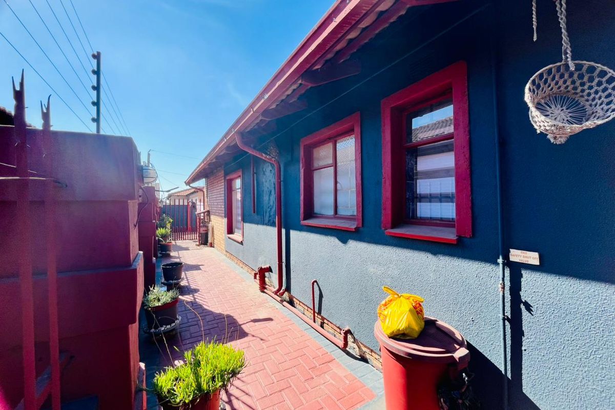 A side exterior walkway featuring paved flooring, red-trimmed window frames, and an external gas shut-off valve.