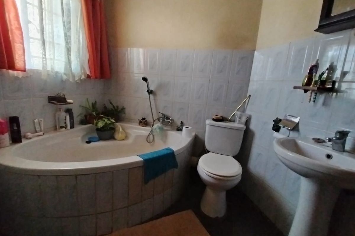 A functional bathroom featuring a corner bathtub, pedestal sink, and toilet with tiled wall finishes.