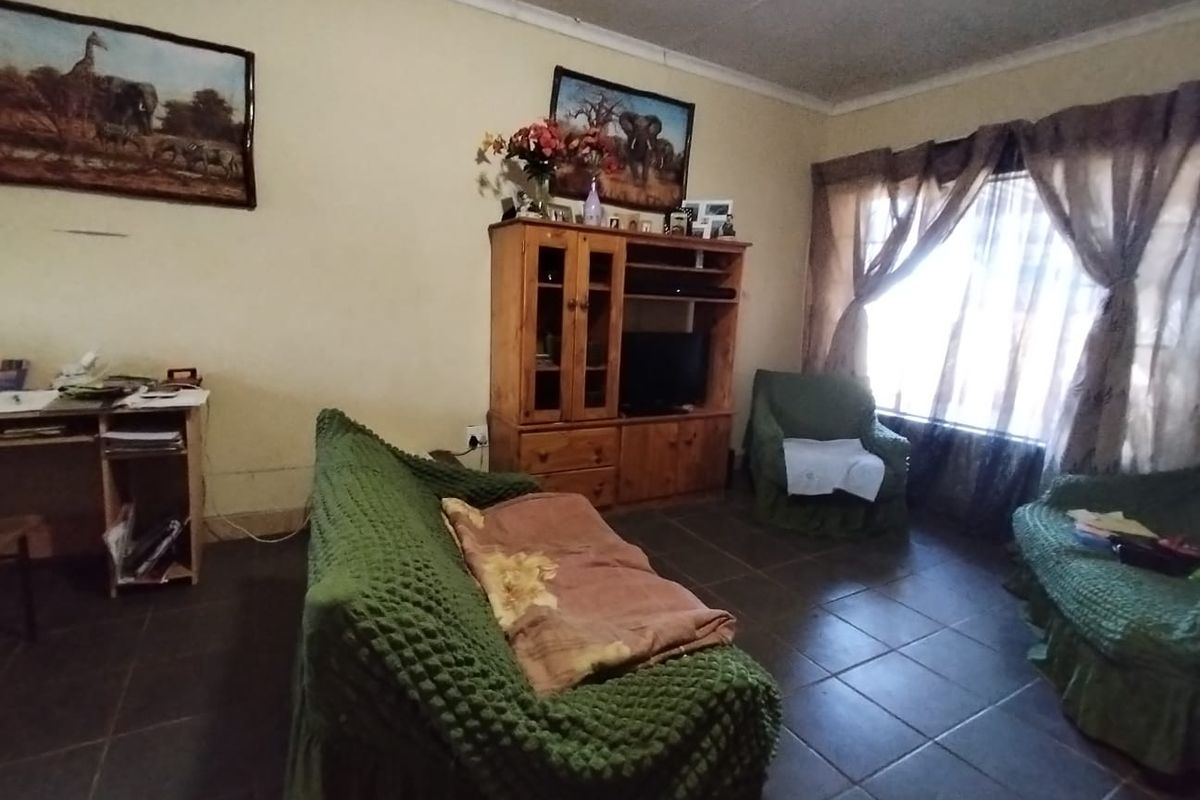 A living room featuring tiled flooring and coved ceilings, currently showing signs of wear and dated finishes.
