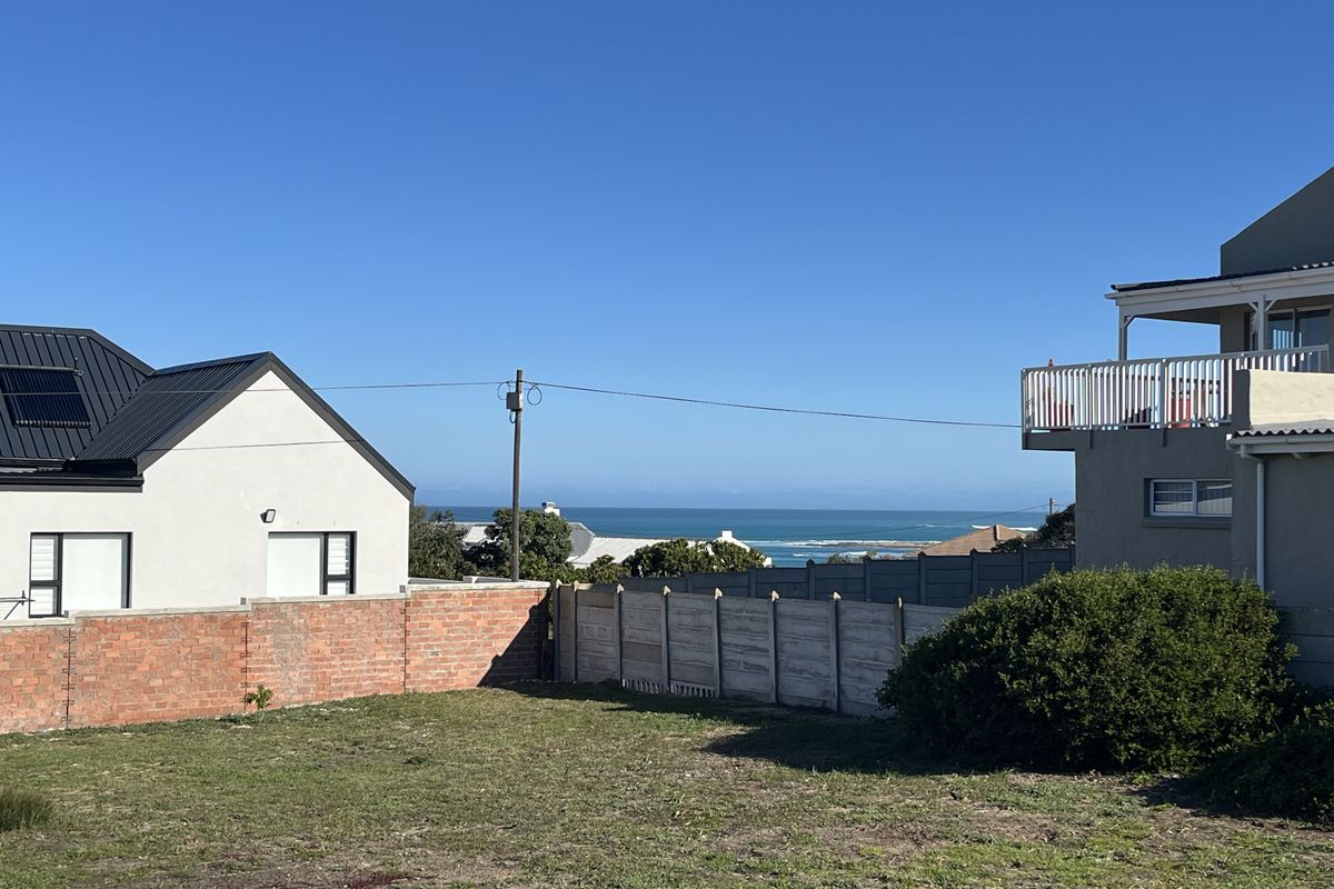 A vacant residential plot featuring a brick boundary wall, precast fencing, and distant ocean views between neighboring properties.