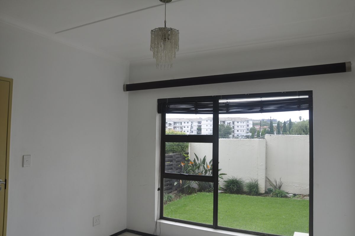 A bright, empty bedroom featuring a large window with views of the garden and surrounding complex.