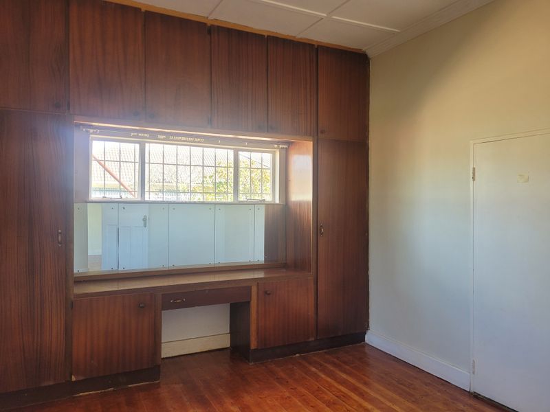 A bedroom featuring extensive built-in wooden cabinetry with an integrated vanity desk, timber flooring, and a window with security bars.