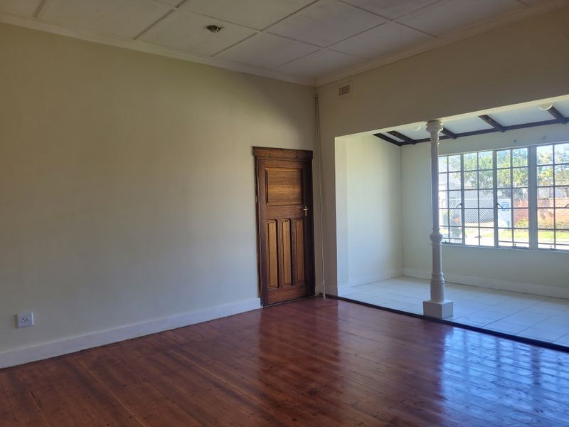 Spacious living area featuring polished hardwood floors, a secondary tiled sunroom space with a decorative column, and classic wooden door detailing.