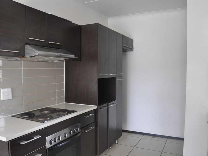 A functional kitchen featuring dark wood cabinetry, a built-in oven with electric hob, stainless steel extractor fan, and neutral tiled backsplash.