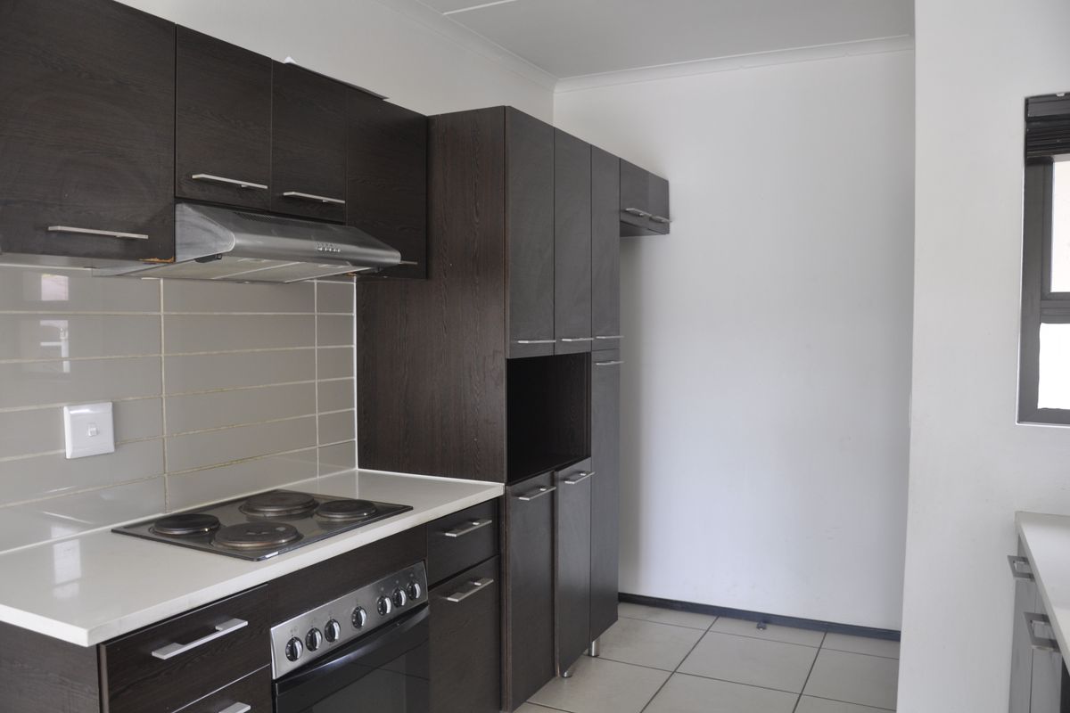 A functional kitchen featuring dark wood cabinetry, a built-in oven with electric hob, stainless steel extractor fan, and neutral tiled backsplash.