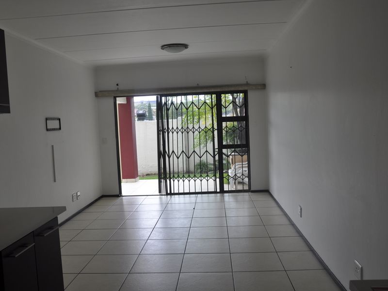 Open plan living area featuring tiled flooring and a sliding security gate leading to an outdoor patio space.