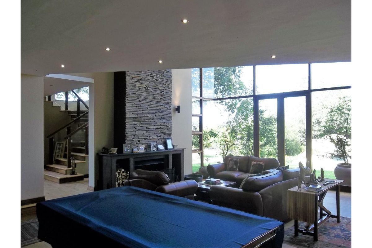 Spacious living area featuring a striking stone-clad fireplace, floor-to-ceiling windows with garden views, and an integrated staircase leading to the upper level.
