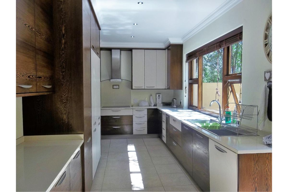 A well-maintained kitchen featuring two-tone cabinetry, stone countertops, a stainless steel extractor fan, and a large window providing natural light.