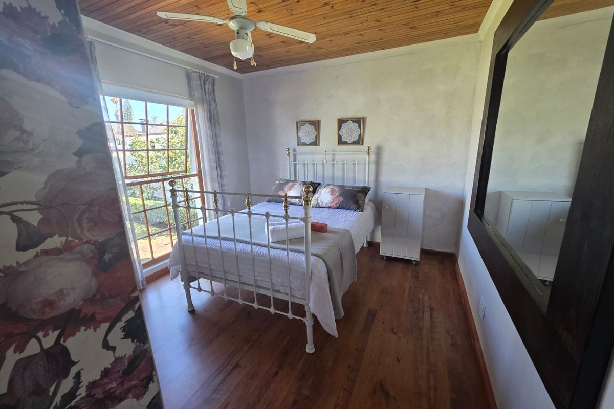 A cozy bedroom featuring warm timber-clad ceilings, rich wood-look flooring, and a large window providing natural light and garden views.