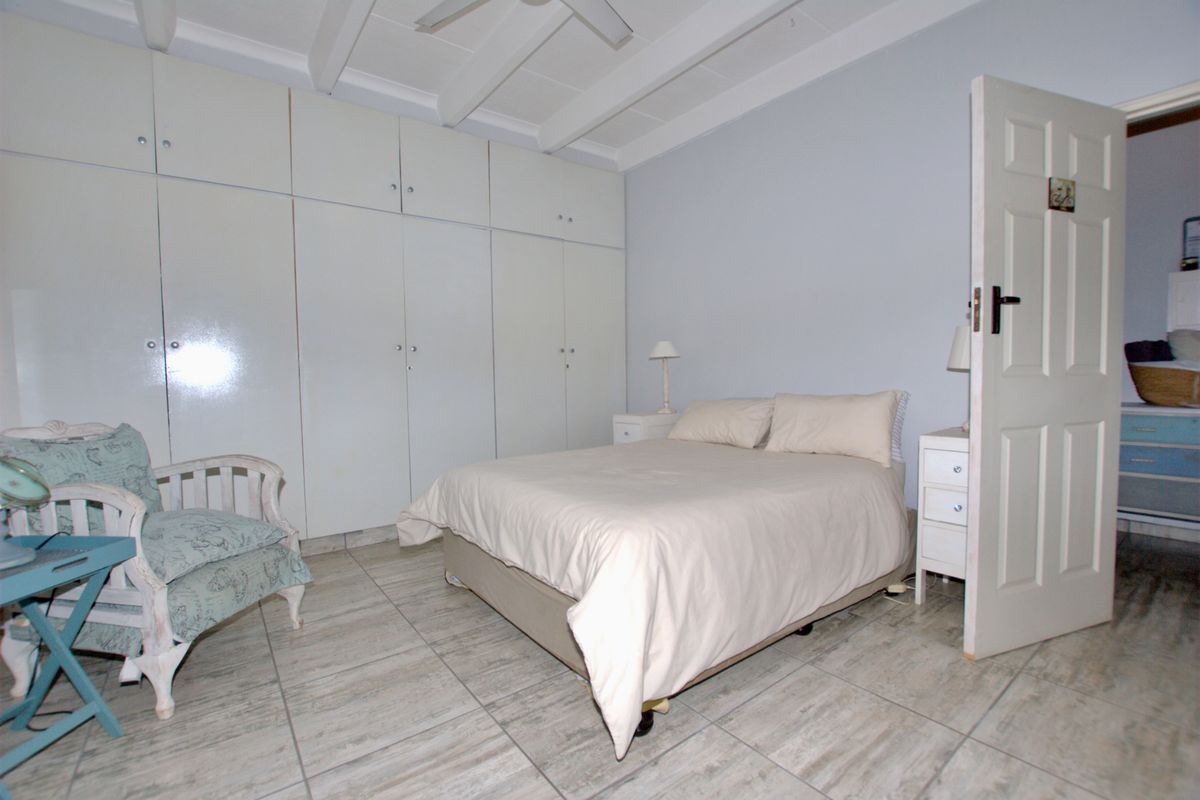 A bedroom featuring built-in cupboards, exposed ceiling beams, and tiled flooring, offering a functional space with potential for modern updates.