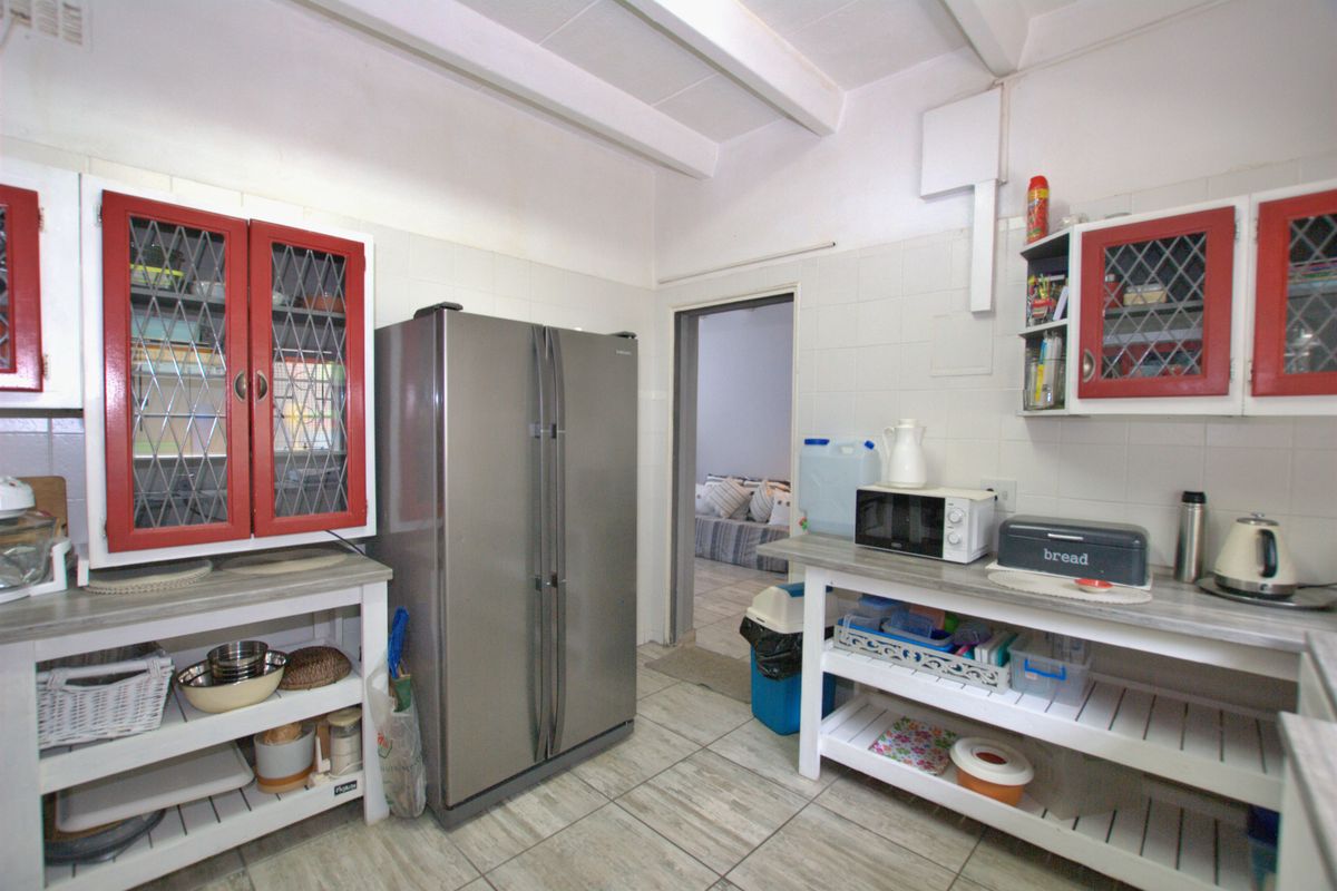 A functional kitchen featuring tiled flooring, wall-mounted cabinetry with red accents, open shelving, and a tiled splashback, leading into an adjacent living area.
