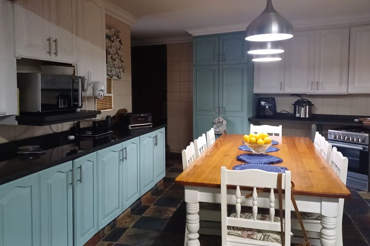 Spacious kitchen featuring a mix of white and blue cabinetry, dark granite countertops, built-in oven, and a central dining area with pendant lighting.