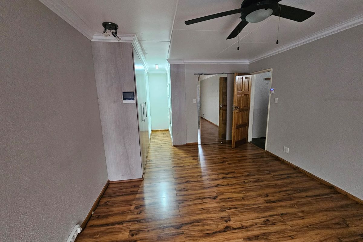 A spacious bedroom featuring wood-look laminate flooring, built-in cabinetry, a ceiling fan, and access to an adjoining room through a wooden door.