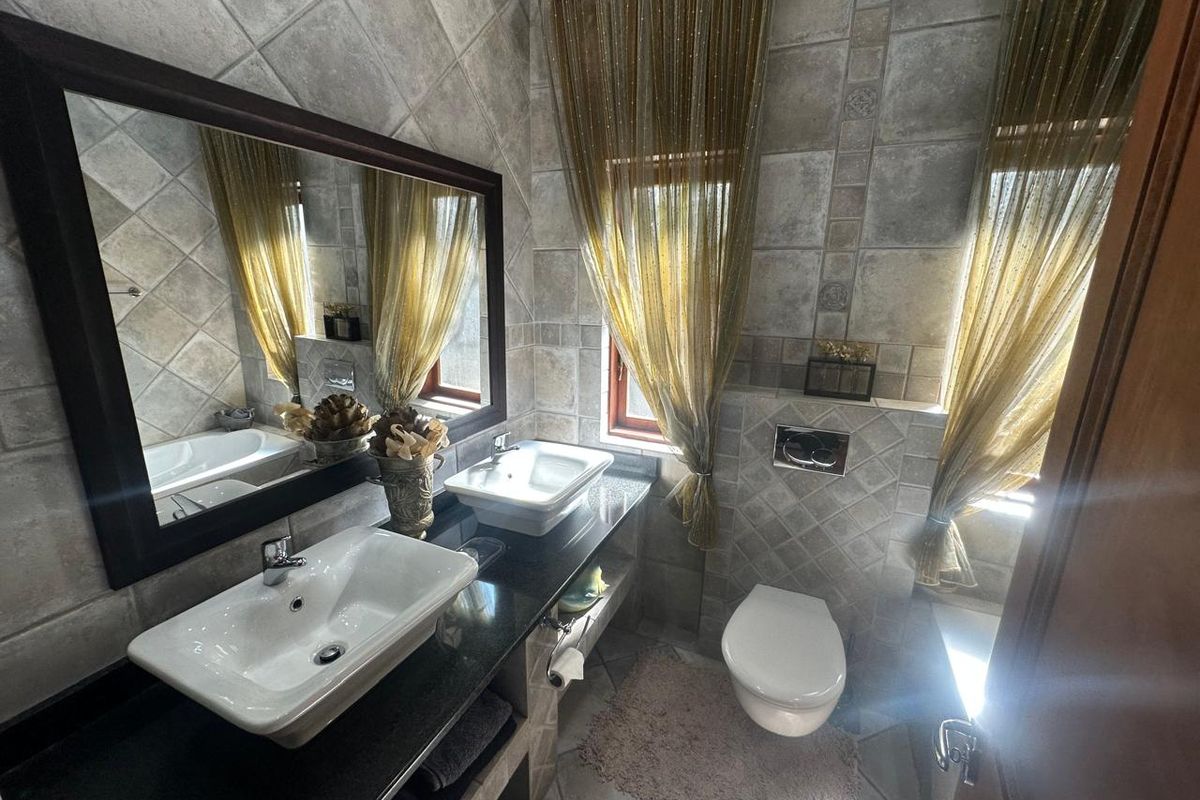 A well-appointed bathroom featuring a double vanity with vessel sinks, granite countertops, and a wall-mounted toilet, finished with neutral stone-look wall and floor tiles.