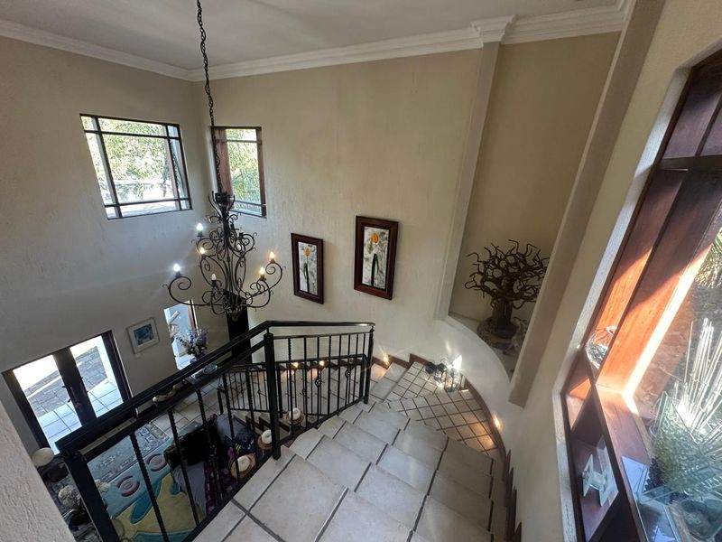A grand double-volume entrance hallway featuring a tiled staircase with wrought iron balustrades, a decorative chandelier, and a built-in wall niche.