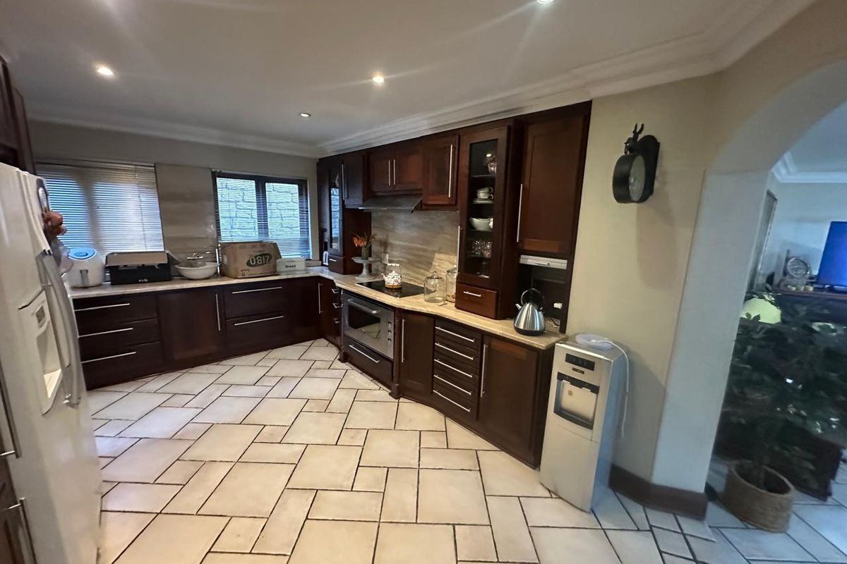 A spacious kitchen featuring dark wood cabinetry, stone countertops, integrated appliances, and tiled flooring with recessed lighting.