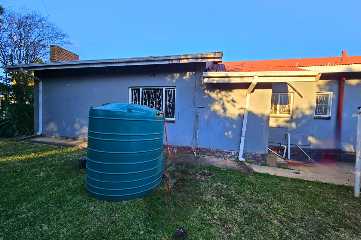 Rear exterior view of the property featuring a water storage tank, lawn area, and visible structural wall cracking.