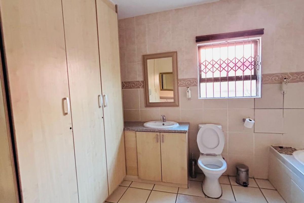 A functional bathroom featuring built-in storage cupboards, a vanity with basin, a toilet, and a bathtub with tiled finishes throughout.