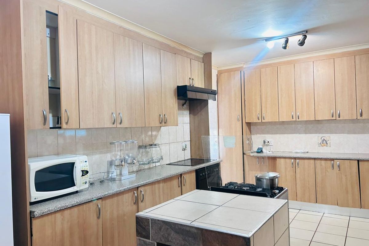 A functional kitchen featuring extensive laminate cabinetry, granite countertops, a tiled backsplash, and a central kitchen island with tiled finish.