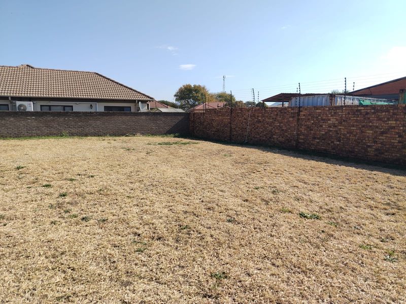 A vacant residential plot featuring a level grass area enclosed by brick boundary walls and fitted with electric fencing.