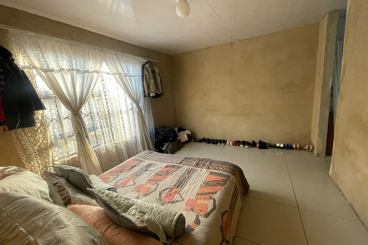 A bedroom featuring tiled flooring and a window with security bars, requiring cosmetic updates to the wall and ceiling finishes.