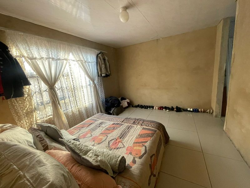 A bedroom featuring tiled flooring and a window with security bars, requiring cosmetic updates to the wall and ceiling finishes.
