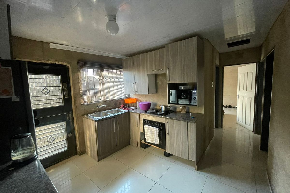 A functional kitchen featuring wood-look cabinetry, a built-in oven and hob, and tiled flooring, requiring finishing touches to the walls and ceiling.