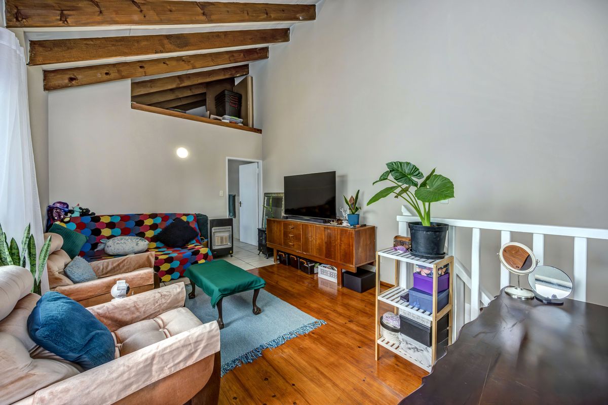 Spacious living area featuring high vaulted ceilings with exposed timber beams, warm timber flooring, and an open mezzanine level overlooking the space.