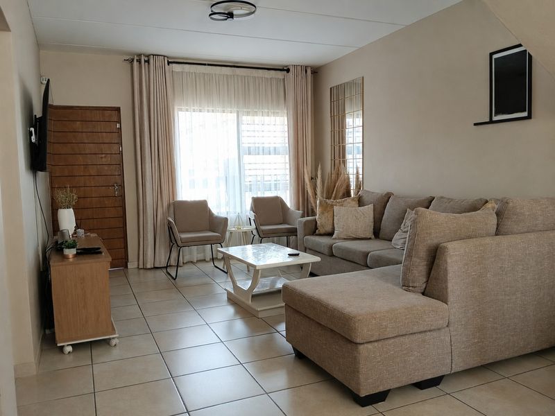 A comfortable living room featuring neutral tiled flooring, large sliding glass doors with curtains, and a functional layout.
