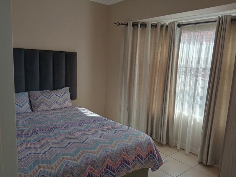 A well-lit bedroom featuring neutral wall tones, tiled flooring, and a large window dressed with curtains.