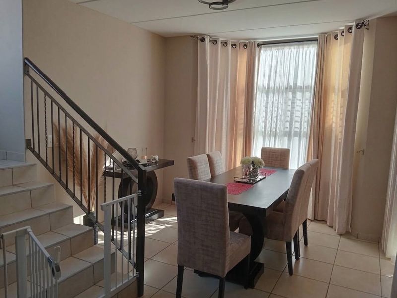 Dining area featuring tiled flooring and a staircase with a metal balustrade, positioned near a large window allowing for natural light.