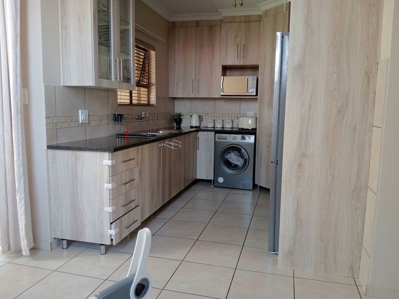 A functional kitchen featuring light wood-grain cabinetry, granite countertops, tiled flooring, and integrated laundry appliances, offering a clean and practical workspace.