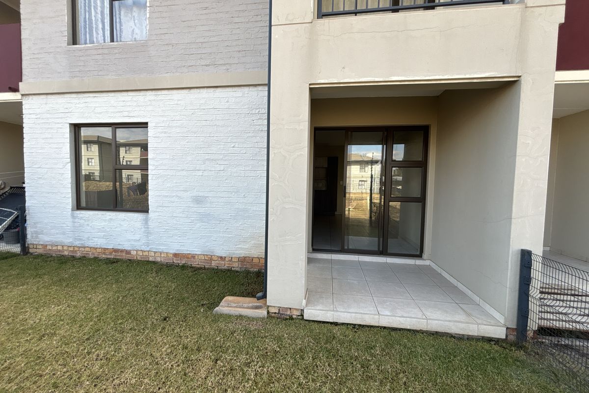 Rear view of the townhouse featuring a covered tiled patio, sliding glass doors, and a small private lawn area.