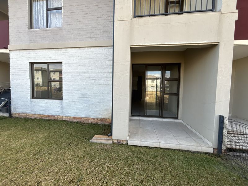 Rear view of the townhouse featuring a covered tiled patio, sliding glass doors, and a small private lawn area.