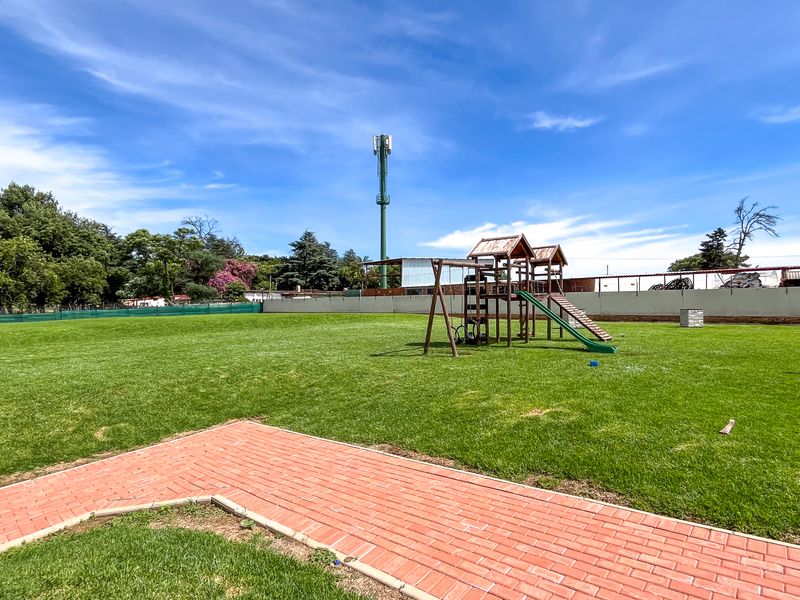 A spacious communal garden area featuring well-maintained lawn, brick paved pathways, and a perimeter boundary wall.