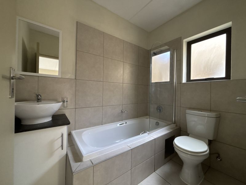 A functional bathroom featuring a built-in bathtub with a glass shower screen, a vessel sink vanity, and neutral wall tiling.