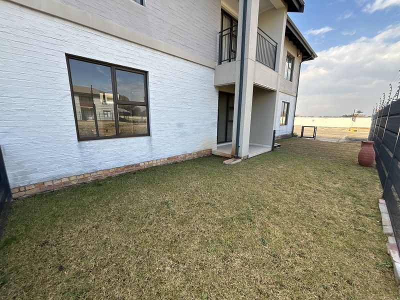 Rear view of a townhouse featuring a painted brick facade, covered patio, upper-level balcony with metal balustrades, and a private lawn area with electric fencing.