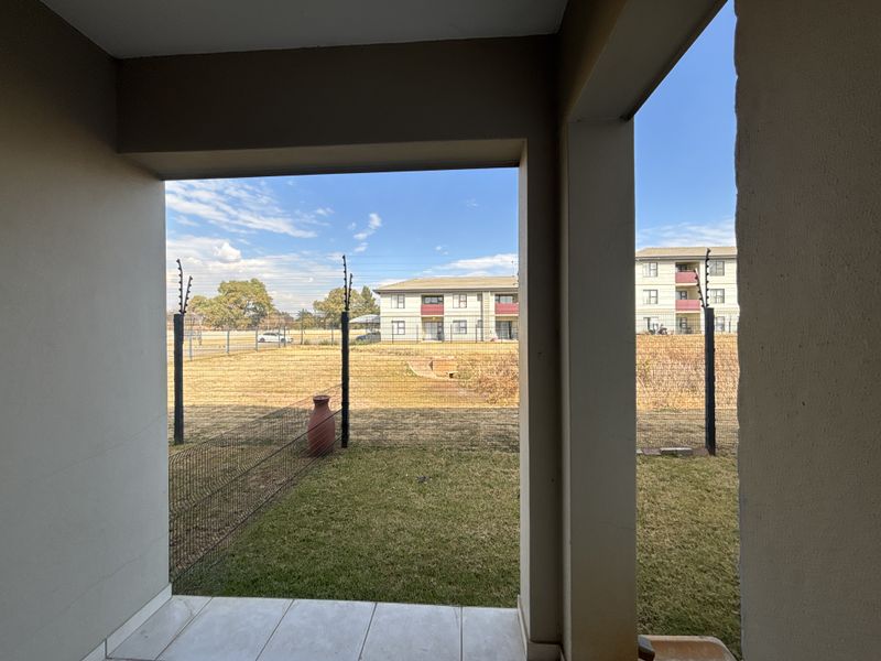 A covered patio area with tiled flooring, overlooking a private garden space enclosed by wire mesh and electric fencing.