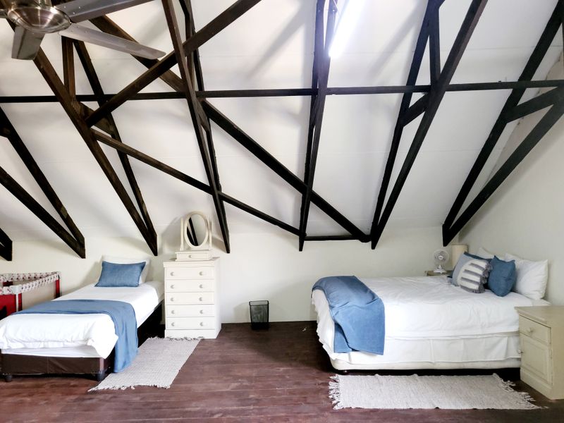 Spacious attic-style bedroom featuring exposed dark timber roof trusses, high vaulted ceilings, and warm timber flooring.
