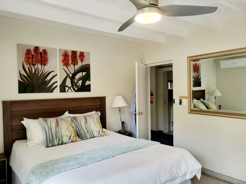 A well-maintained bedroom featuring exposed beam ceilings, a ceiling fan, and a wall-mounted air conditioning unit for climate control.