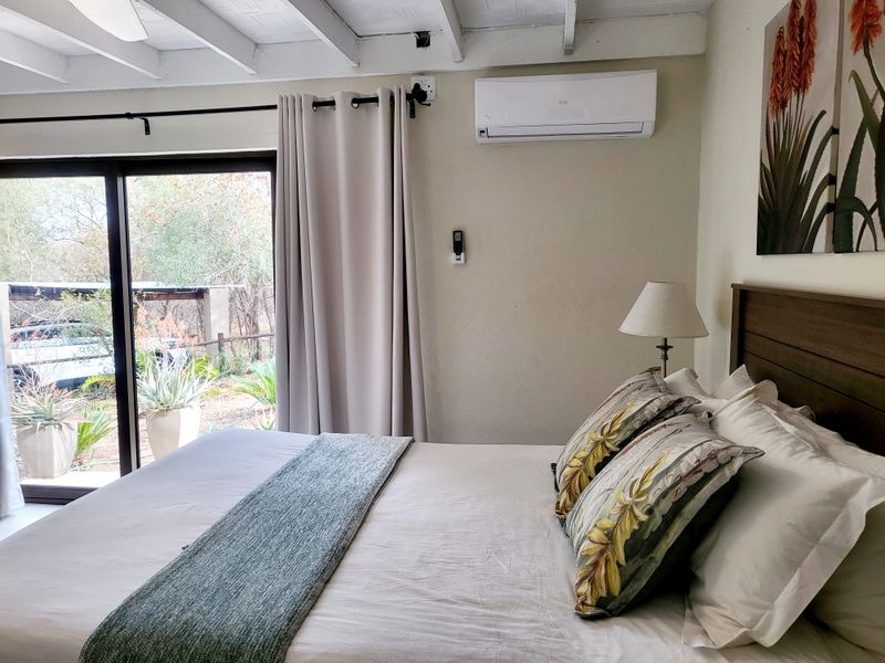 A comfortable bedroom featuring exposed beam ceilings, a wall-mounted air conditioning unit, and large sliding glass doors providing access to the outdoor area.