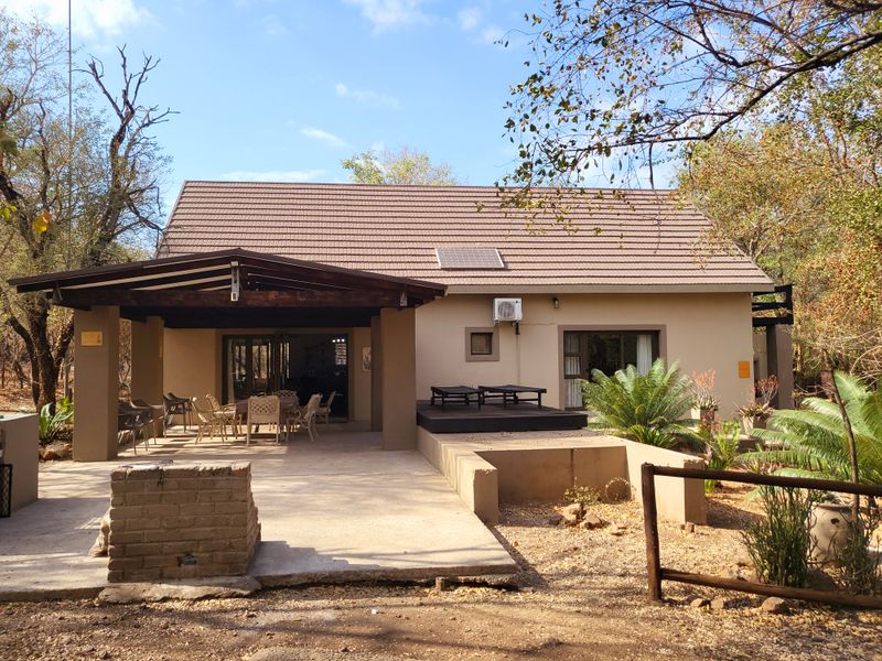 Rear view of the house featuring a covered patio, timber decking, brick braai area, and a tiled roof with a solar panel.