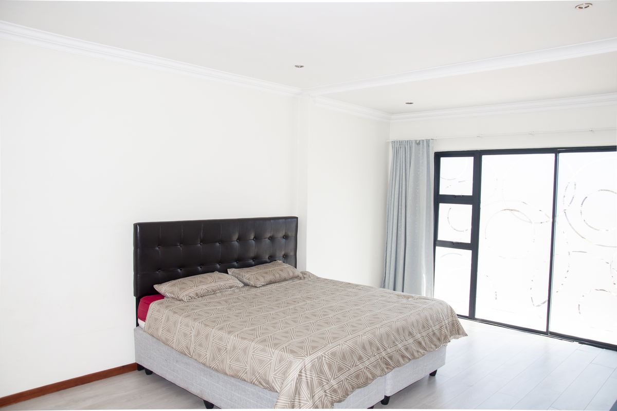 A bright and spacious bedroom featuring neutral walls, crown molding, light-toned flooring, and large sliding glass doors providing ample natural light.