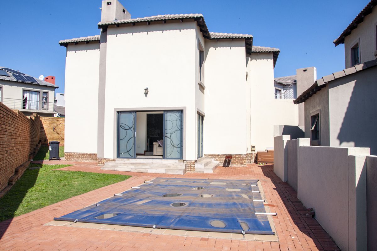 Rear view of the property featuring a paved patio area, a swimming pool with a safety cover, and a well-maintained exterior facade.