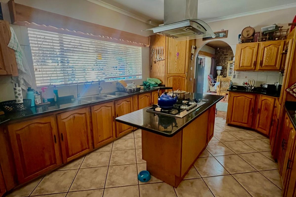 A traditional kitchen featuring wooden cabinetry, granite countertops, a central island with a gas hob, and tiled flooring.