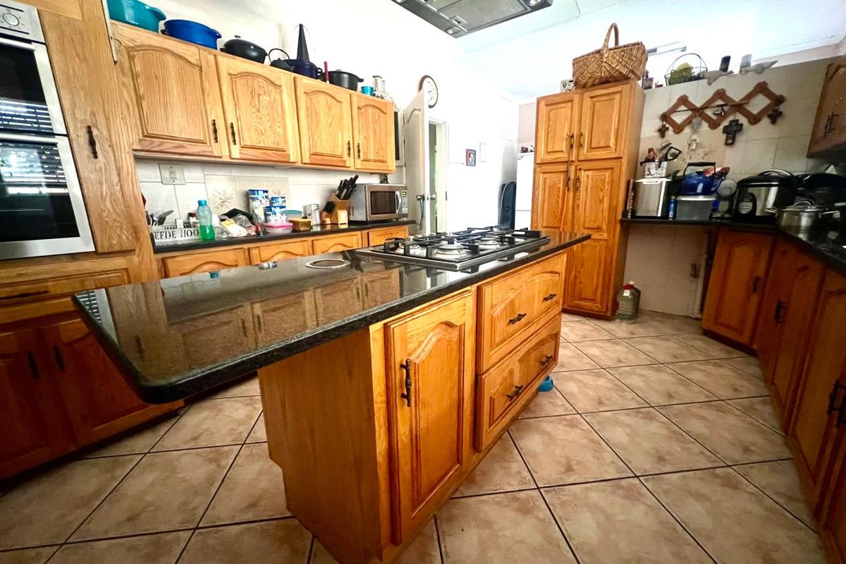Spacious kitchen featuring traditional wooden cabinetry, granite countertops, a central island with a gas hob, and tiled flooring throughout.