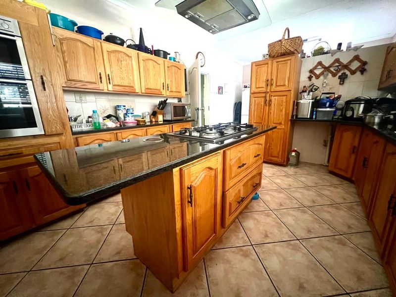 Spacious kitchen featuring traditional wooden cabinetry, granite countertops, a central island with a gas hob, and tiled flooring throughout.