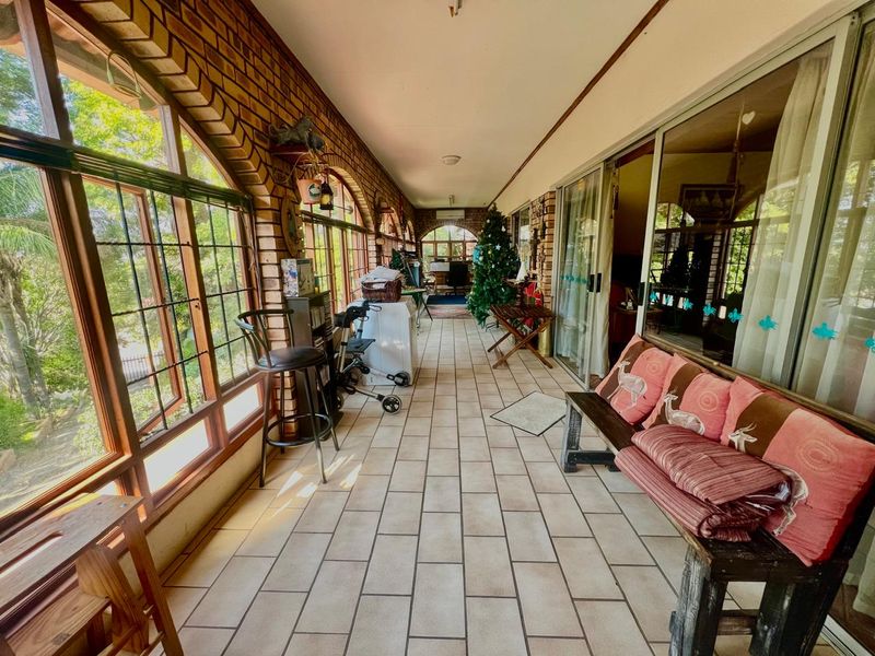 A covered patio area featuring exposed brick walls, tiled flooring, and large arched windows, providing a bright transition space between the interior and garden.