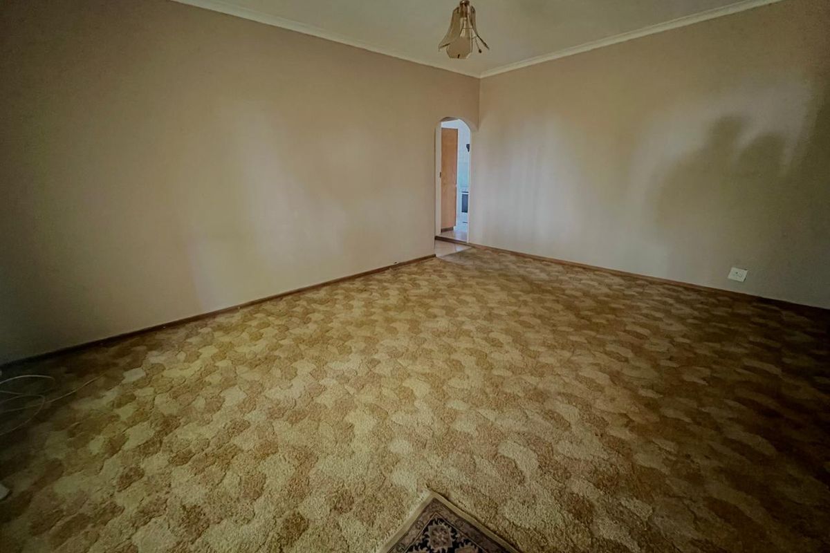 A spacious, empty living room featuring dated wall-to-wall carpeting and a classic arched doorway leading to an adjacent room.