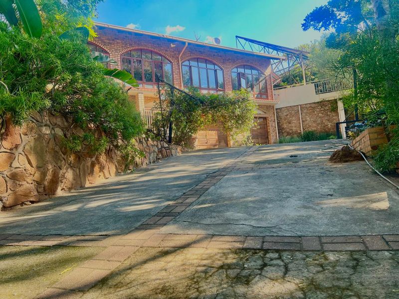 Front view of a multi-level brick house featuring arched windows, a concrete driveway, and stone retaining walls set within a landscaped garden.